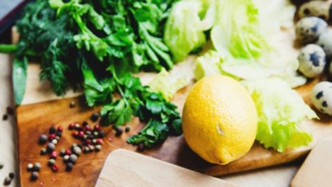 Frischer Kabeljau auf einem Holzbrett, umgeben von Gemüse, Kräutern und einer Zitrone, ideal für gesunde Rezepte.