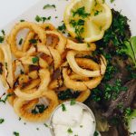 Frittierte Calamari-Ringe mit frischer Zitrone und Kräutern, serviert mit einer Dip-Sauce auf einem weißen Teller.