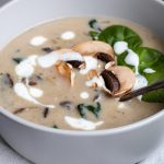 Eine Schüssel mit cremiger Pilzsuppe, Spinat und frischen Champignons, garniert mit Sahne. Ideal für eine herzhafte Mahlzeit.