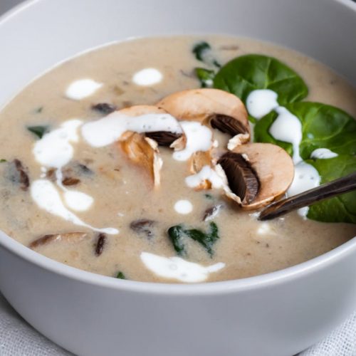 Eine Schüssel mit cremiger Pilzsuppe, Spinat und frischen Champignons, garniert mit Sahne. Ideal für eine herzhafte Mahlzeit.