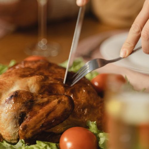Geröstetes Hähnchen auf einem Tisch, umgeben von frischem Gemüse und Tomaten, bereit zum Servieren, mit Besteck zum Schneiden.