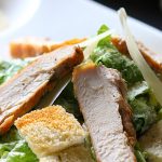 Frischer Hähnchensalat mit knusprigen Croutons und Parmesan, serviert auf einem weißen Teller.