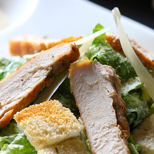 Frischer Hähnchensalat mit knusprigen Croutons und Parmesan, serviert auf einem weißen Teller.