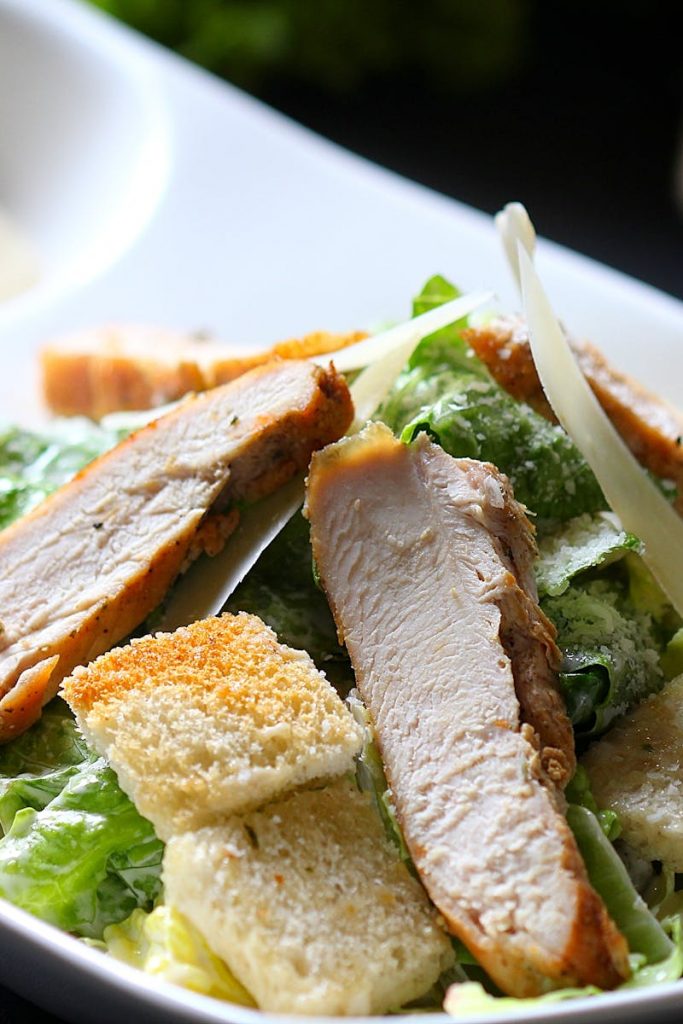 Frischer Hähnchensalat mit knusprigen Croutons und Parmesan, serviert auf einem weißen Teller.