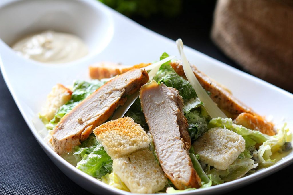 Frischer Hähnchensalat mit Caesar-Dressing, Croutons und grünen Blättern auf einem weißen Teller.