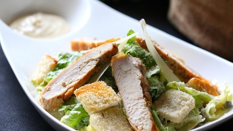 Frischer Hähnchensalat mit Caesar-Dressing, Croutons und grünen Blättern auf einem weißen Teller.