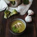 Eine Schüssel mit Bärlauch-Cremesuppe, garniert mit Brokkoliröschen und Knoblauchzehen auf einem Holztisch.