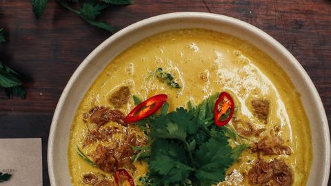 Eine cremige Humus-Suppe mit frischen Kräutern, roten Chilischoten und knusprigen Zwiebelstücken in einer Schüssel.