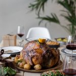 Geröstetes Hähnchen auf einem Tisch mit Beilagen, Rotwein und Dekoration, ideal für festliche Anlässe und Familienessen.