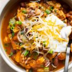 Eine Schüssel mit herzhaftem Eintopf, garniert mit Käse, Sahne und Frühlingszwiebeln, ideal für eine nahrhafte Mahlzeit.