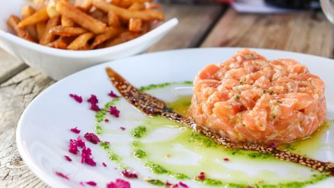 Frisches Lachs-Tatar auf einem weißen Teller mit Pommes frites und dekorativen Kräutern, ideal für Feinschmecker und Fischliebhaber.