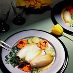 Gekochter Chicorée auf einem Teller mit Karotten, Zucchini und einer Sauce, serviert mit Gläsern und Dekoration.