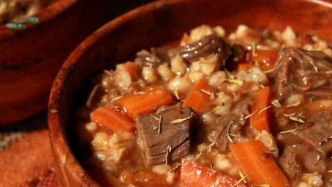 Herzhafter Eintopf aus Fleisch, Karotten und Gerste in einer Holzschüssel, ideal für eine nahrhafte Mahlzeit.