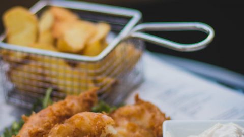 Frittierte Fischfilets mit Limette und Dip auf einem Teller, serviert mit knusprigen Kartoffelstücken.