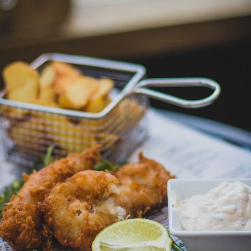 Frittierte Fischfilets mit Limette und Dip auf einem Teller, serviert mit knusprigen Kartoffelstücken.