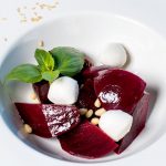 Ein Rote-Bete-Salat mit Feta, frischem Basilikum und Pinienkernen auf einem weißen Teller.