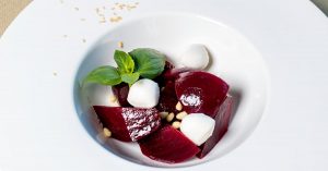 Ein Rote-Bete-Salat mit Feta, frischem Basilikum und Pinienkernen auf einem weißen Teller.