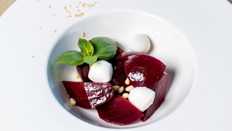 Ein Rote-Bete-Salat mit Feta, frischem Basilikum und Pinienkernen auf einem weißen Teller.