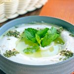 Eine cremige Joghurtsuppe mit frischer Minze und Kräutern, serviert in einer grauen Schüssel, ideal für verschiedene Gerichte.