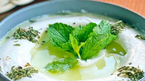 Eine cremige Joghurtsuppe mit frischer Minze und Kräutern, serviert in einer grauen Schüssel, ideal für verschiedene Gerichte.