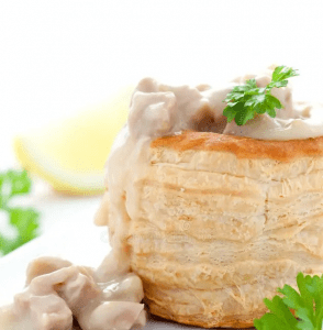 Blätterteig-Törtchen gefüllt mit Hähnchen und einer cremigen Sauce, garniert mit frischen Kräutern und Zitrone.