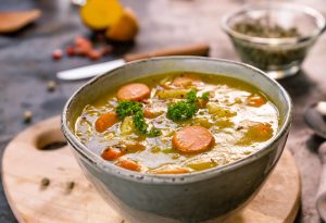 Eine Schüssel mit Erbseneintopf, gefüllt mit Karotten, Brokkoli und weiteren Gemüsesorten, serviert in einer modernen Schüssel.