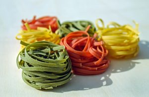 Bunte Pasta-Nudeln in Spiralen, bestehend aus grünen, roten, gelben und orangefarbenen Fäden, auf einem hellen Untergrund.