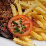 Ein saftiges Steak mit karamellisierten Zwiebeln, serviert mit knusprigen Pommes Frites und einer Scheibe Tomate mit Petersilie.