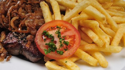 Ein saftiges Steak mit karamellisierten Zwiebeln, serviert mit knusprigen Pommes Frites und einer Scheibe Tomate mit Petersilie.