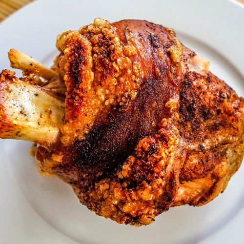 Krustenschweinebraten mit knuspriger Haut, serviert auf einem weißen Teller, ideal für Fleischliebhaber und Feinschmecker.