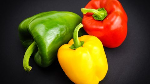 Drei Paprika in verschiedenen Farben: grün, rot und gelb, auf schwarzem Hintergrund, ideal für Rezepte und gesunde Ernährung.