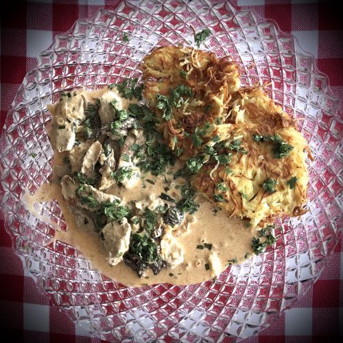 Ein Teller mit zarten Fleischstücken in Sahnesauce und knusprigen Kartoffelpuffern, garniert mit frischen Kräutern.