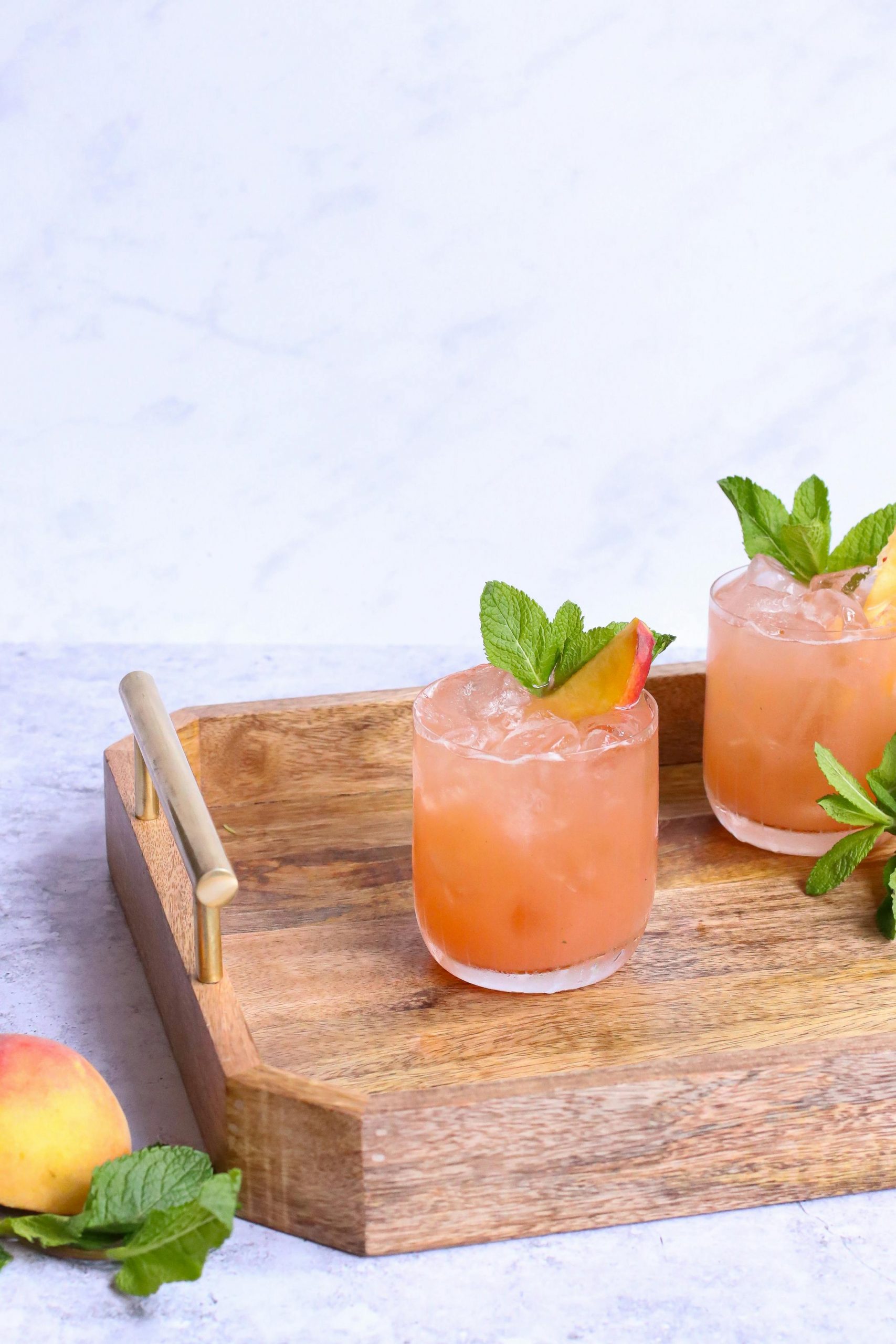 Glasses of tasty alcoholic drinks decorated with fresh peach slices and mint leaves on wooden tray