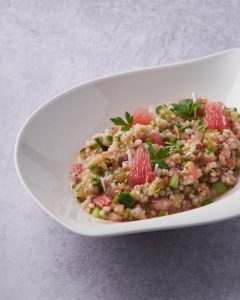 Ein frischer Couscous-Salat mit Grapefruit, Gurken und Kräutern in einer weißen Schüssel, ideal für gesunde Ernährung.