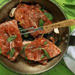 Gegrillte Fleischscheiben mit frischen Kräutern in einer Pfanne, ideal für Fleischliebhaber und Kochrezepte.