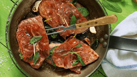 Gegrillte Fleischscheiben mit frischen Kräutern in einer Pfanne, ideal für Fleischliebhaber und Kochrezepte.