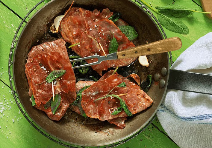 Gegrillte Fleischscheiben mit frischen Kräutern in einer Pfanne, ideal für Fleischliebhaber und Kochrezepte.