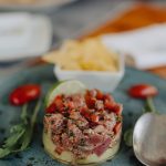 Ein Teller mit Gourmet-Tatar, serviert mit Chips, Kirschtomaten und frischen Kräutern auf einem blauen Teller.