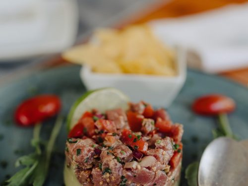 Ein Teller mit Gourmet-Tatar, serviert mit Chips, Kirschtomaten und frischen Kräutern auf einem blauen Teller.