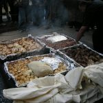 Ein traditionelles Festmahl im Freien mit verschiedenen Fleisch- und Teiggerichten, die auf einem Tisch serviert werden.