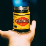Vegemite Hefeextrakt in einem Glas mit gelbem Etikett, 220g, Produkt aus Australien, auf einer Hand gehalten.