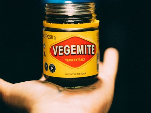 Vegemite Hefeextrakt in einem Glas mit gelbem Etikett, 220g, Produkt aus Australien, auf einer Hand gehalten.