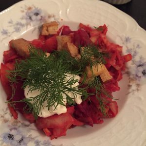 Ein traditionelles Gemüsegericht mit roten Rüben, Dill, Croutons und Sauerrahm auf einem dekorativen Teller.