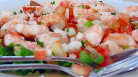 Frischer Garnelen-Salat mit Tomaten, Zwiebeln und Kräutern auf einem weißen Teller, serviert mit Besteck.