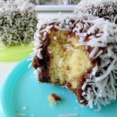 Ein Stück Kokos-Schokoladenkuchen mit einer Bissstelle, umhüllt von Kokosraspeln und Schokoladenglasur.