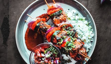 Gegrillte Spieße mit Gemüse, Reis und verschiedenen Saucen auf einem Teller, ideal für Feinschmecker und Grillliebhaber.