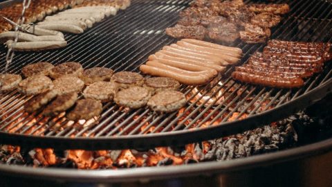 Ein Grill mit einer Auswahl an Würstchen, Burgern und mariniertem Fleisch auf dem Rost, ideal für Grillabende und BBQ-Events.