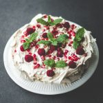 Himbeer-Minz-Torte mit Granatapfelkernen auf einem weißen Teller, dekoriert mit frischen Minzblättern und Himbeeren.