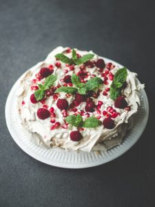 Himbeer-Minz-Torte mit Granatapfelkernen auf einem weißen Teller, dekoriert mit frischen Minzblättern und Himbeeren.