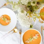 Schalen mit cremiger Suppe und frischen Kräutern, dekoriert mit einem Blumenarrangement auf einem Tisch.